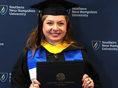 Marjory Nolasco Ramirez, who earned her BS in Business Administration in 2024 from SNHU, wearing her cap and gown and holding her diploma.