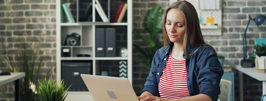 A woman sitting at a table typing on a laptop in an office setting.