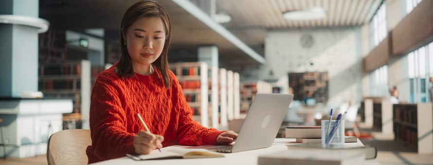 A student in a red sweater using a laptop, pen and notebook to brainstorm what she can do with a master's in English.