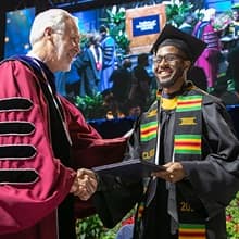Matthew Seawright in cap and gown, receiving his degree from President Paul LeBlanc at SNHU's Commencement.