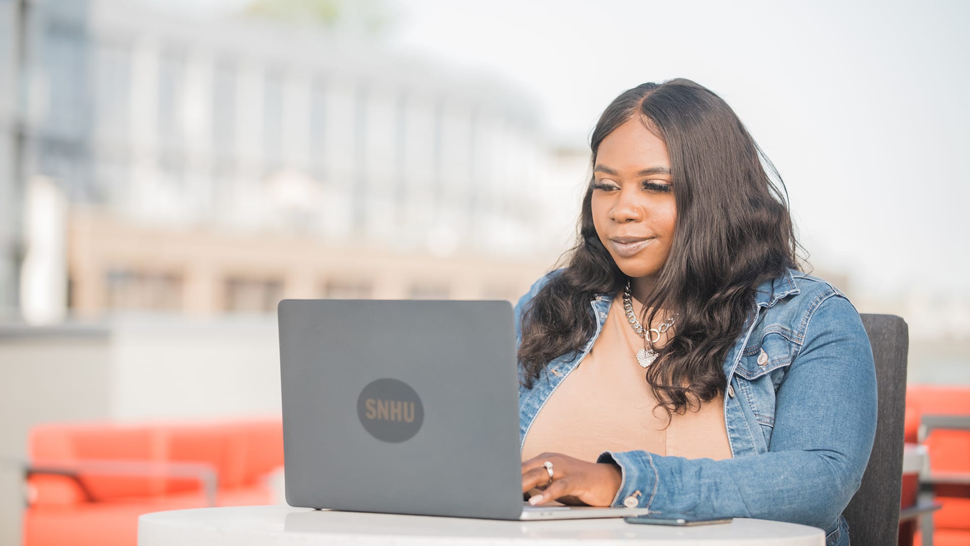 Tanzania Fair, who earned a degree in 2020, wearing a denim jacket and working on her laptop with an SNHU sticker on the front.