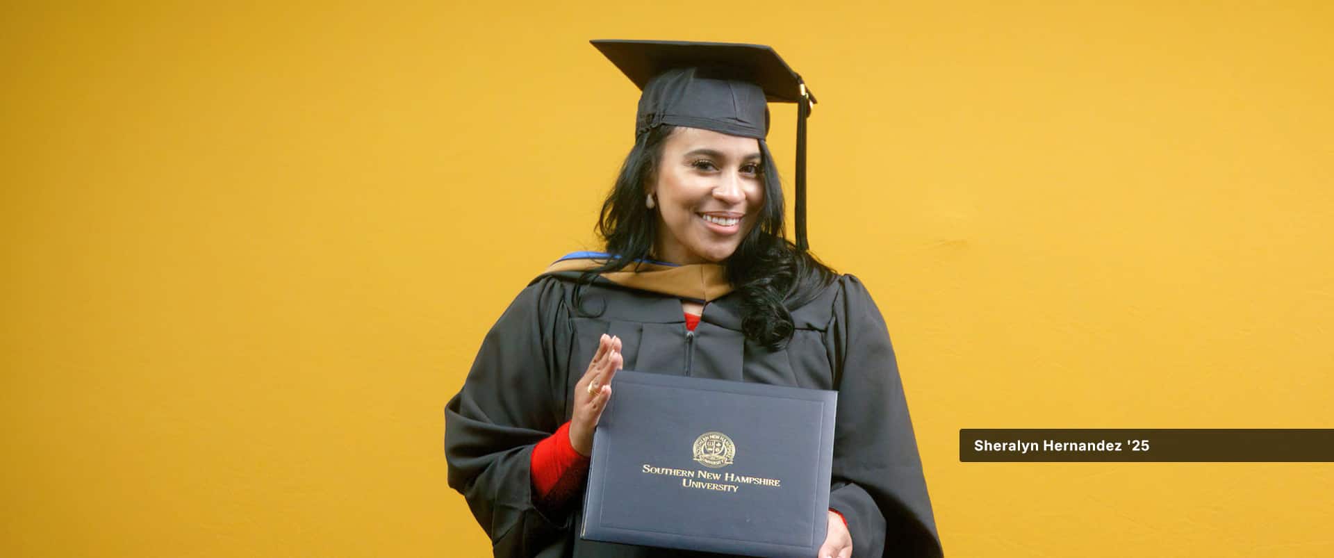 Sheralyn Hernandez, who earned her MBA in healthcare management from SNHU in 2024, wearing her cap and gown and holding her diploma in front of a yellow backdrop.