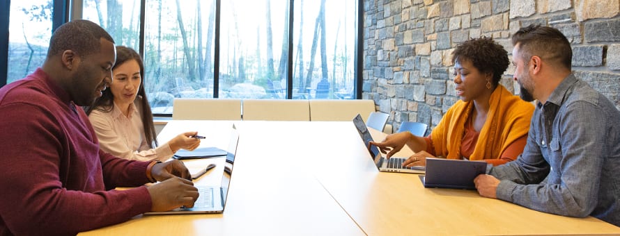 Four business professionals working in pairs at a conference table, discussing MBA vs MS degrees. 