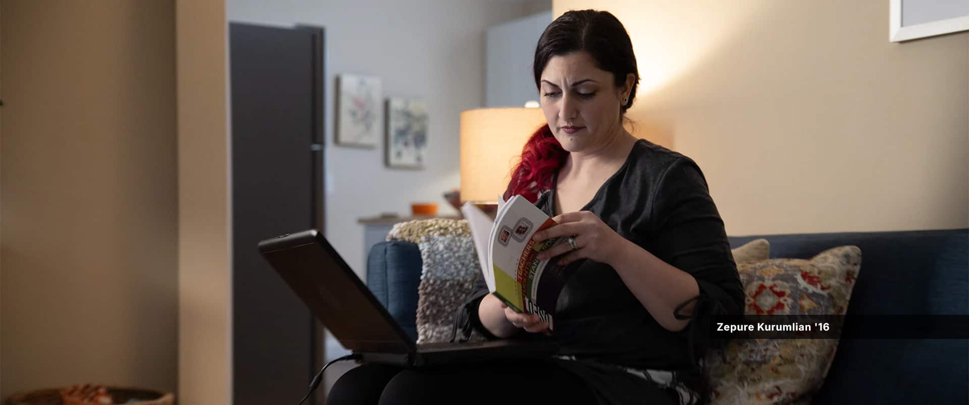 Zepure Kurumlian, who earned her degree from SNHU in 2016, thumbing through a book while sitting on a couch in her living room with a laptop on her lap.