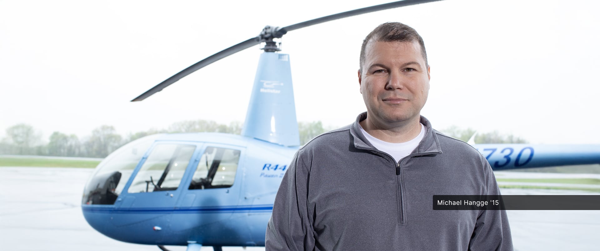 Michael Hangge, an SNHU alum, standing in front of a helicopter wearing a grey zipped sweatshirt.