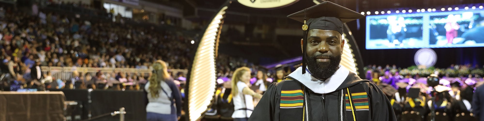 Cedric Parker holding his diploma and wearing his graduation cap and gown at the SNHU commencement ceremony.