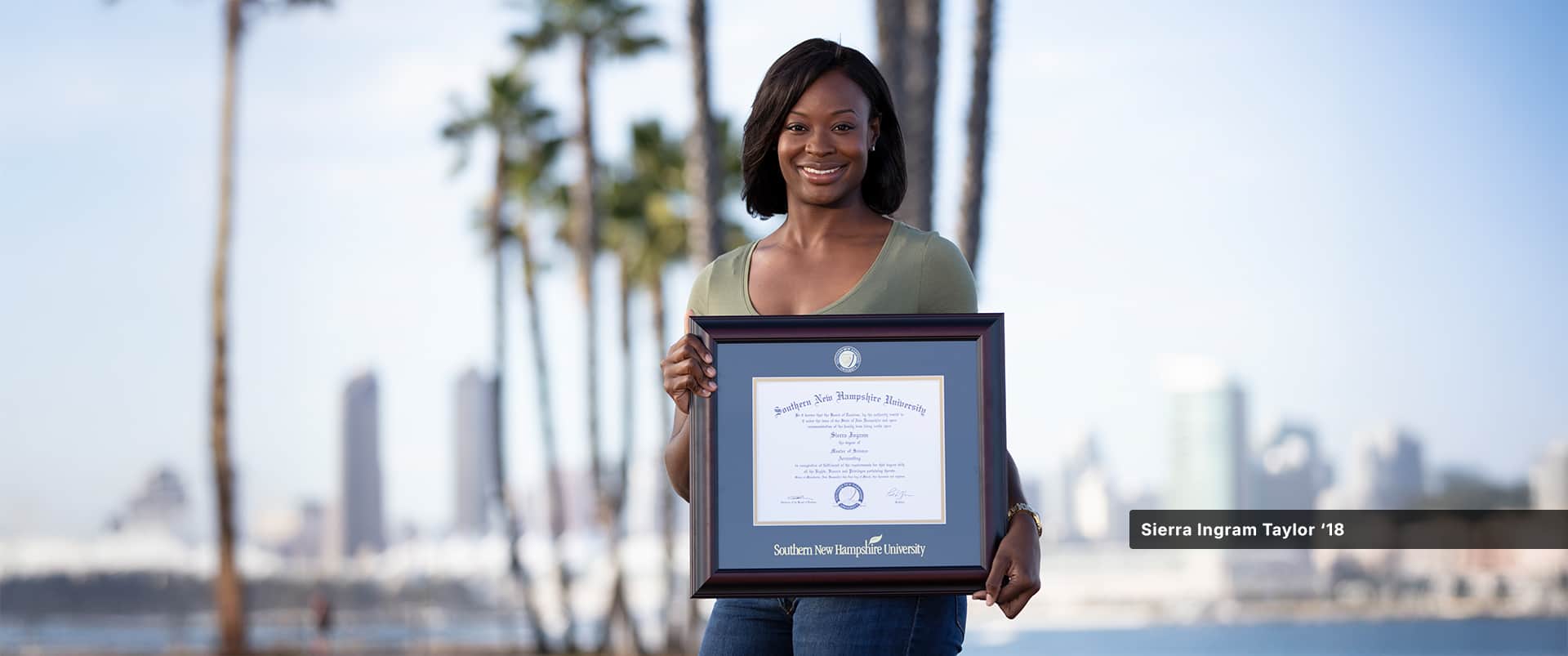 Sierra Ingram Taylor, who earned her master's in accounting from SNHU in 2018, wearing a green t-shirt and jeans and holding her framed diploma.