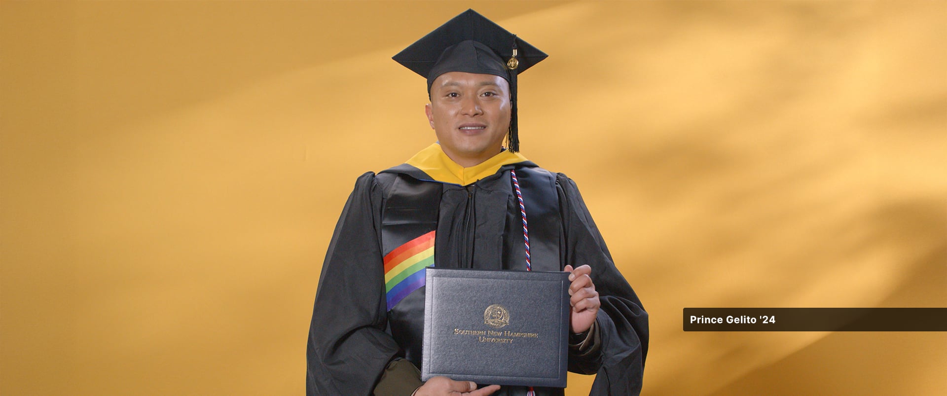 Prince Gelito, who earned his master's in cybersecurity from SNHU in 2024, wearing his cap and gown and holding his diploma.