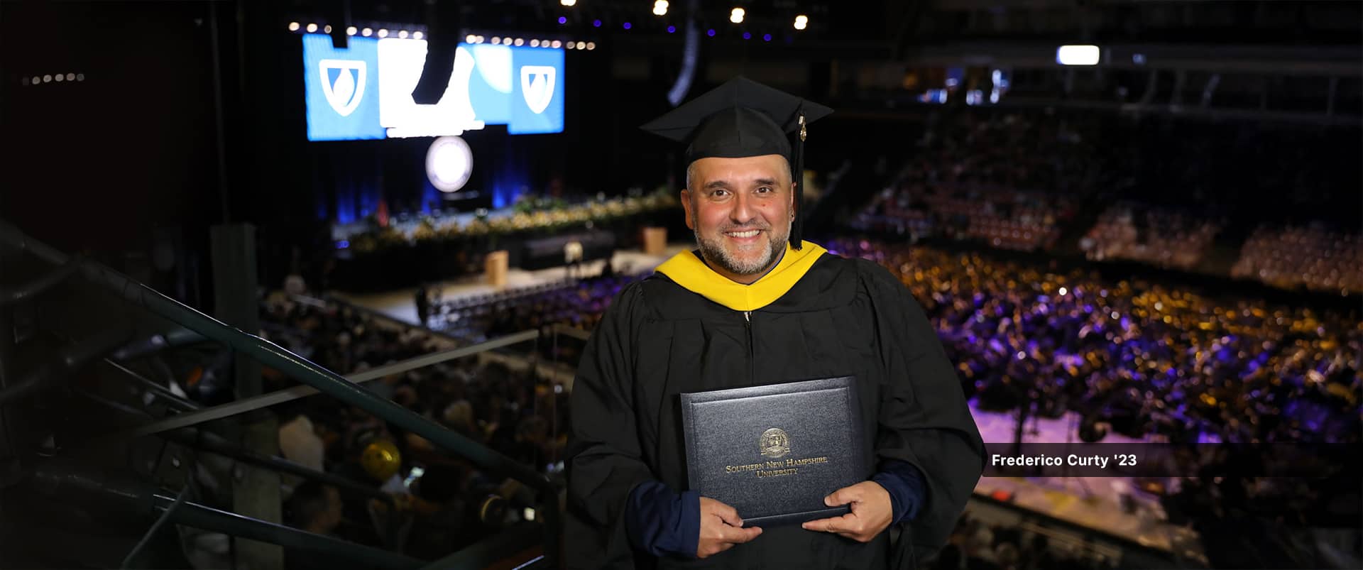 Frederico Curty, who earned his master's in higher education administration from SNHU in 2023, wearing his cap and gown and holding his diploma.