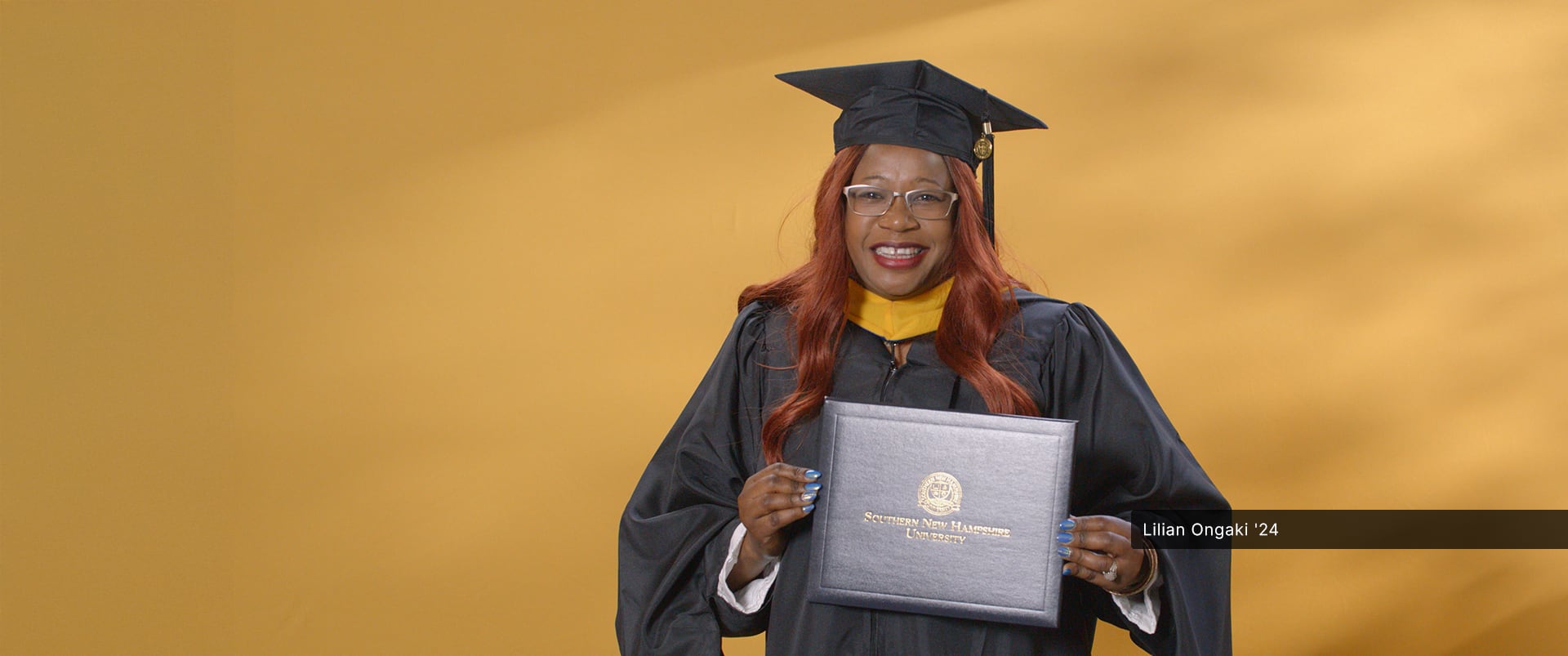Lilian Ongaki, who earned her master's in human resource management from SNHU in 2024, wearing her cap and gown and holding her diploma. 