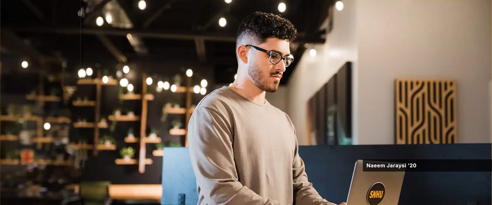 Naeem Jaraysi, who earned a marketing degree in 2021, standing and working on a laptop with an SNHU sticker on the front.