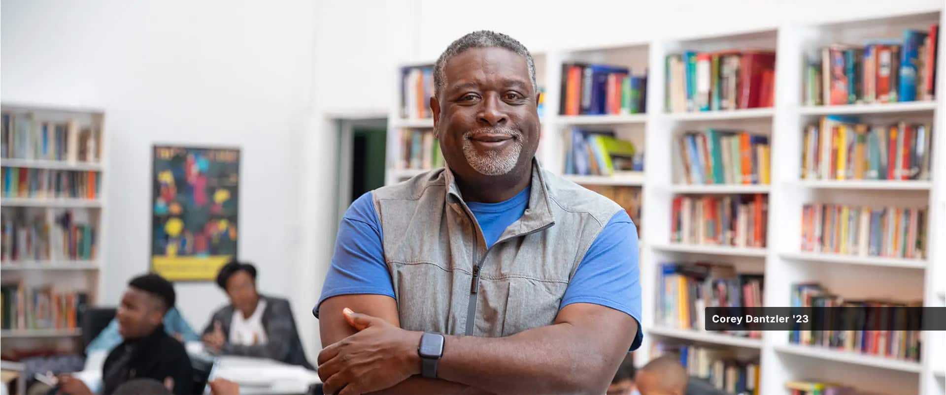 Corey Dantzler, who earned his degree from SNHU in 2023, wearing a grey vest and blue T-shirt, with 3 kids and several bookshelves in the background.