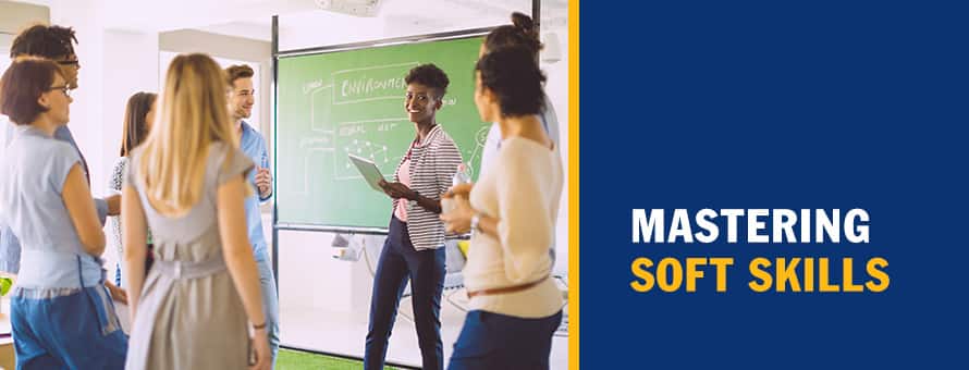 A group of people listening to a woman standing next to a chalk board and holding a tablet and the text Mastering Soft Skills..
