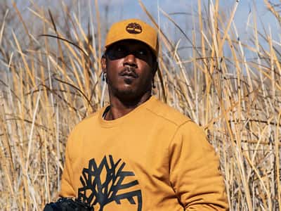 Ryan Carter, an online photography student at SNHU, wearing a yellow hat and sweatshirt, standing in a field of tall grass.