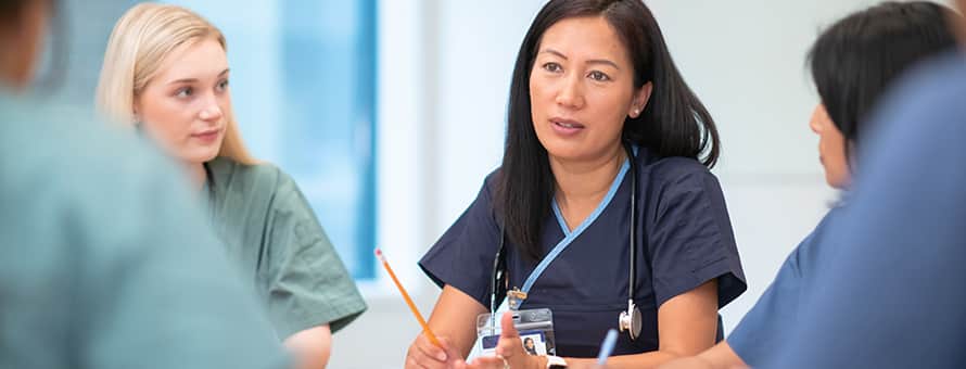 A nurse leader with a stethoscope, leading a meeting with a group of other nurses