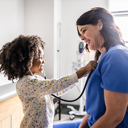 A child testing a stethoscope on her nurse, who has the nursing acronym RN