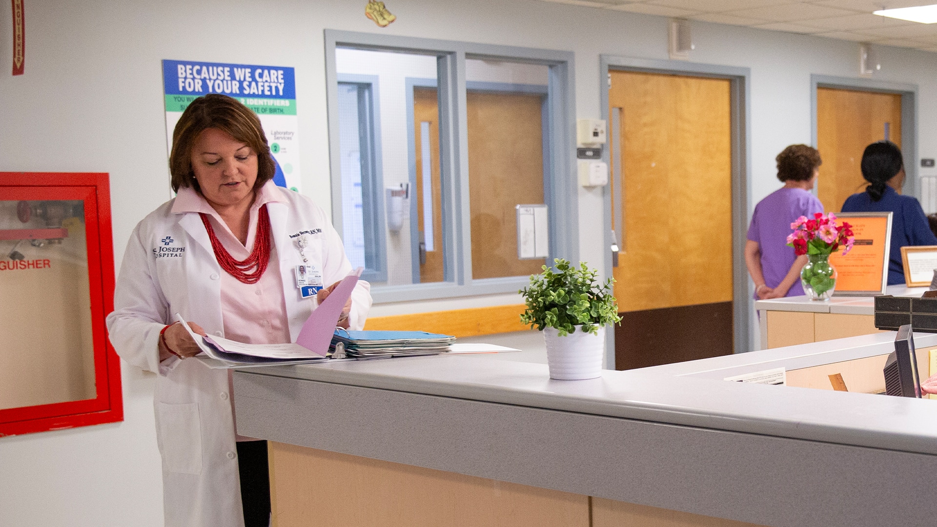 Bonnie Fecowicz, who earned her degree from SNHU, wearing a white lab coat in a hospital reading papers in  an open folder she's holding
