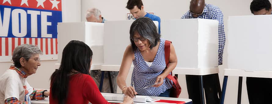 A woman registering to vote with voting booths behind her.