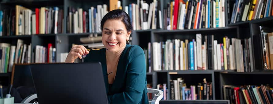 A woman sitting in front of a bookshelf full of books working on her laptop