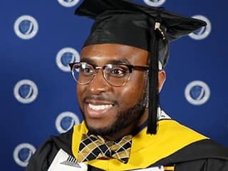 Rakia Green, who earned his master's in healthcare administration from SNHU in 2023, wearing his cap and gown, eyeglasses and a bow tie. 