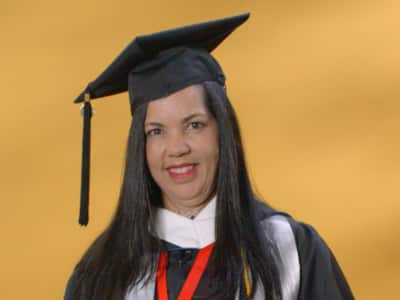 Regina Dacruz Reis, who earned her bachelor's in psychology, from SNHU in 2024, wearing her cap and gown and holding her diploma.