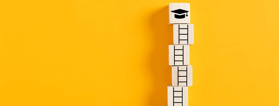 A stack of five building blocks on a yellow backdrop: the bottom four blocks feature pieces of a ladder and the top depicts a graduation cap