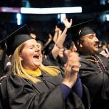 Shelly and Sal Villa wearing their cap and gowns, clapping and cheering at SNHU's commencement.