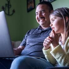 Sal Villa working on his laptop while his daughter looks on.