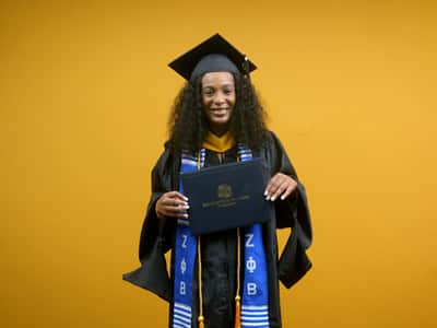 Shiqueta Dixon, who earned her online master's in healthcare administration from SNHU in 2025, wearing her cap and gown and holding her diploma in front of a yellow backdrop.