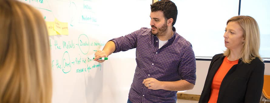  Two project managers working together, using a white board to discuss which project management methodology would be best for their objective.