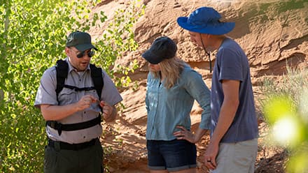 John Roos, who attended college online at Southern New Hampshire University, in his role as a park ranger guiding tourists by a wall of rock and shrubbery.