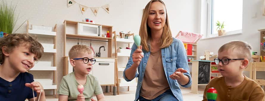  A teacher and a group of young students sitting on the floor, playing musical instruments.