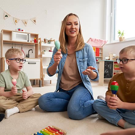  A teacher and a group of young students sitting on the floor, playing musical instruments.