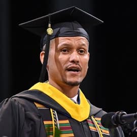 Andreas Galatis standing in front of a micorphone, delivering his SNHU Commencement address