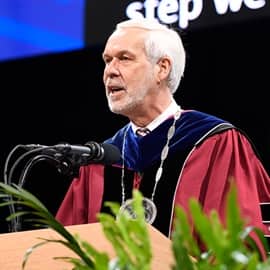 SNHU President Paul LeBlanc standing behind a podium at Commencement, addressing the audience.
