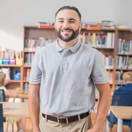Stephen Goulakos, a 2022 graduate from SNHU with a BA in Psychology and a concentration in Mental Health, standing in a classroom with kids working at their desks.