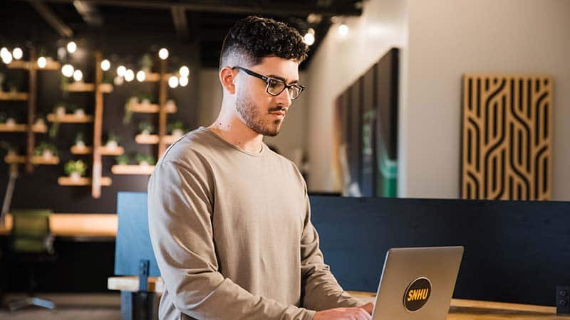 A SNHU student standing at a desk while using thier computer.