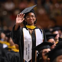 Tanner McCarthy standing and waving during her SNHU commencement ceremony, wearing her first-generation stole.