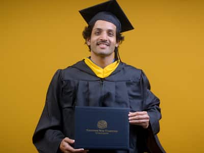Tarun Vijjali, who earned his online bachelor's business administration with a concentration in management Information systems from SNHU in 2025, wearing his cap and gown and holding his diploma in front of a yellow backdrop.