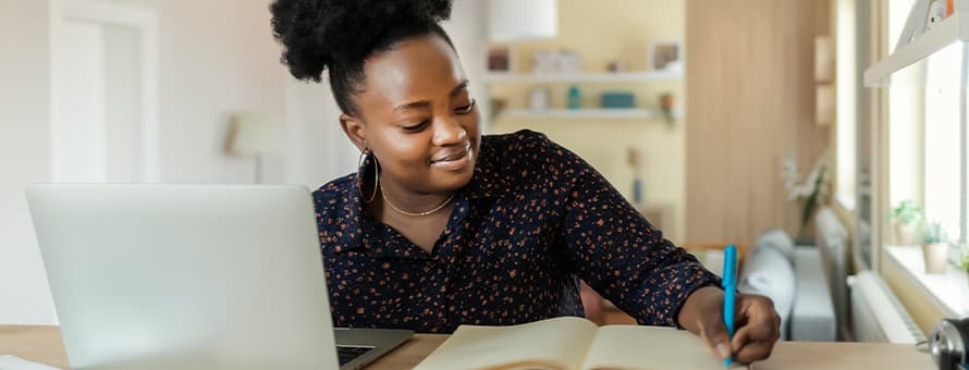 A person sitting in front of a laptop, writing in a notebook about the types of bachelor’s degrees she can choose from.