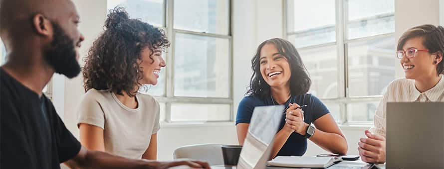 A group of smiling professionals sat around a conference table with laptops and documents.