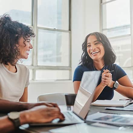 A group of smiling professionals sat around a conference table with laptops and documents.