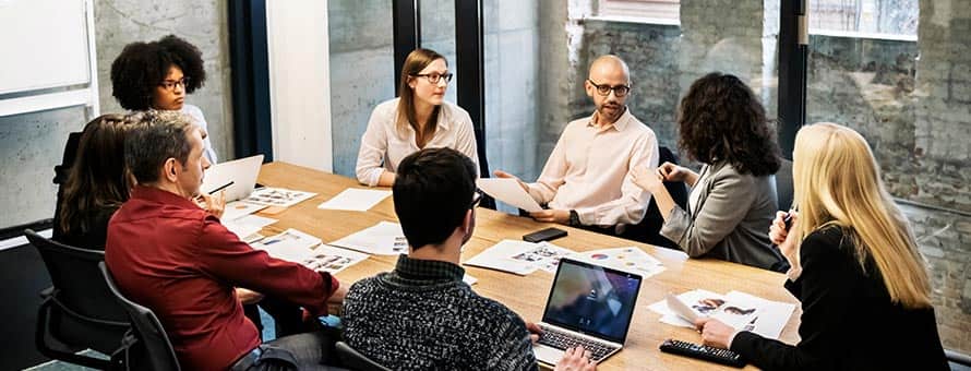 A group of men and women sitting around a conference room table working in their role as digital marketer