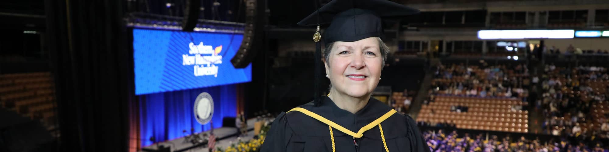 Pam Dulmage, a Vermont resident, wearing her cap and gown and holding her diploma at the SNHU commencement.