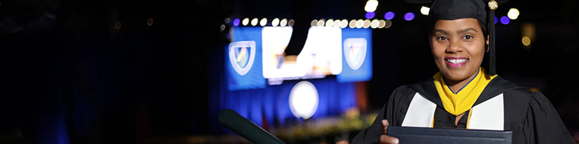Eleshia Louis, an SNHU grad and Virginia resident, in her cap and gown and holding her diploma inside a large arena.