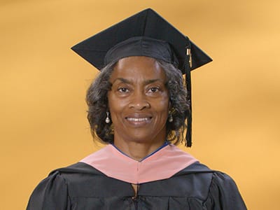Wanda Edwards, who earned her Master of Public Health degree in 2024, wearing her cap and gown in front of a yellow backdrop.