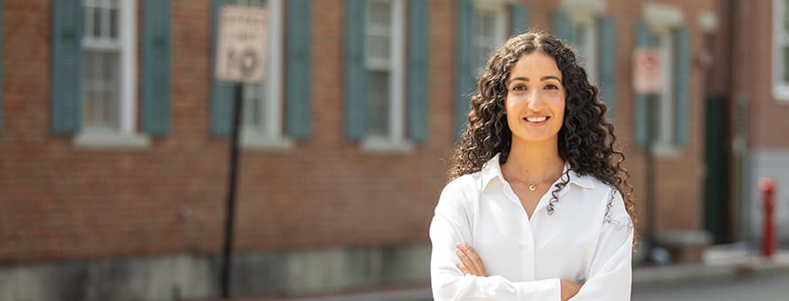 Fatma Salem Pease, 2019 graduate of SNHU's MA in Clinical Mental Health Counseling, standing smiling with arms folded in front of a brick building.