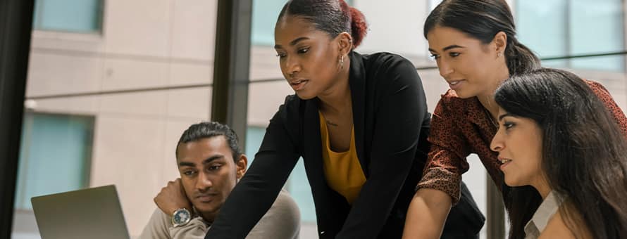Four professionals with business degrees reviewing information on a laptop.