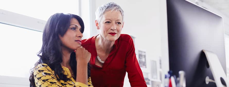 Two women sitting in front of a desktop while considering what you can do with an MBA