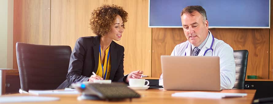 A public health professional discussing a project with a doctor as they both look at a laptop